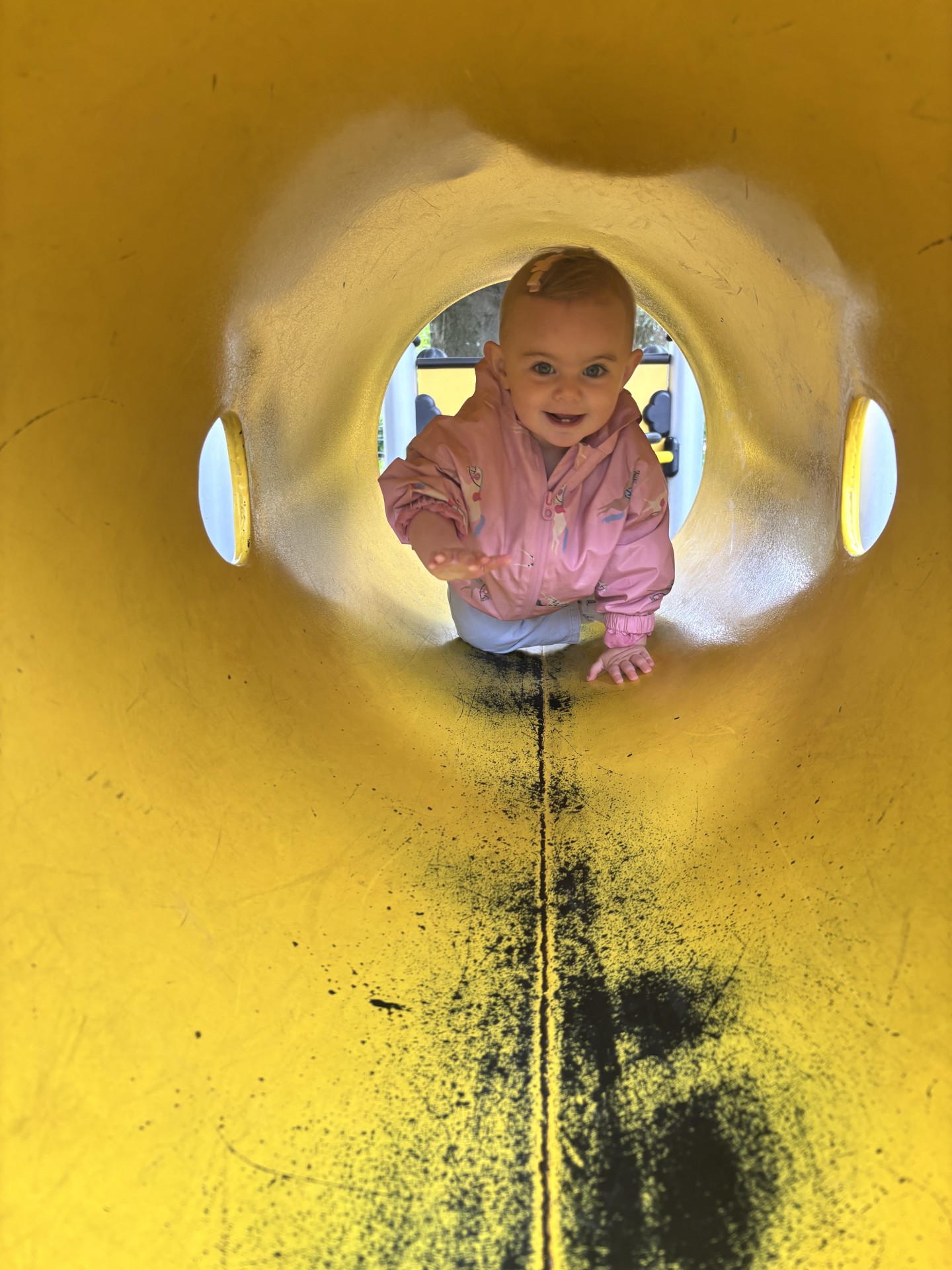 Smiling toddler crawling through a yellow play tunnel